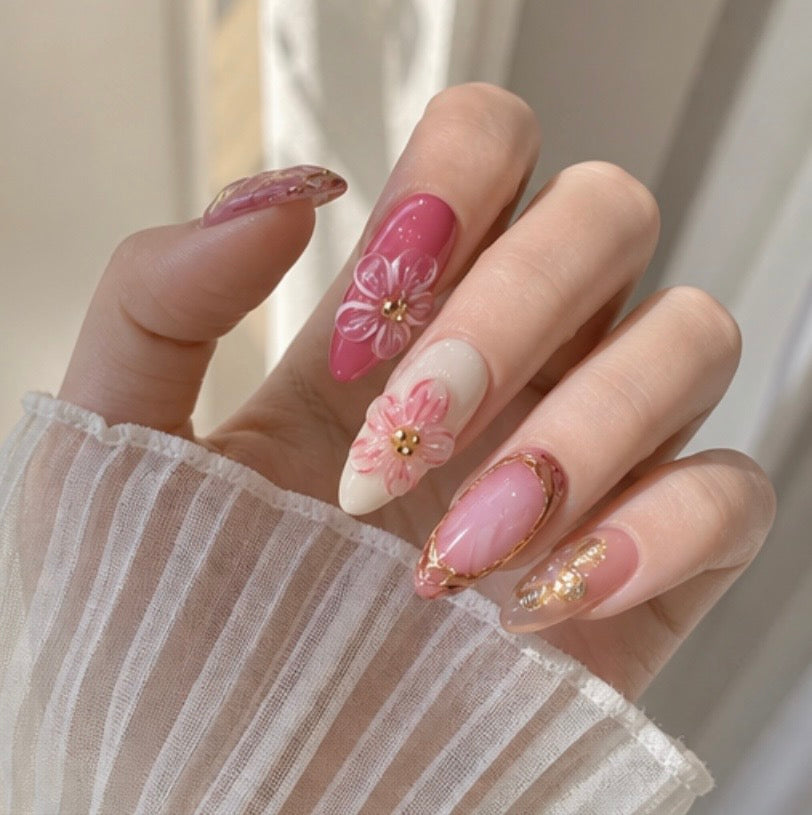 Hand wearing almond press-on nails – pink ombré with 3D floral details and gold accents – Lande Accessories